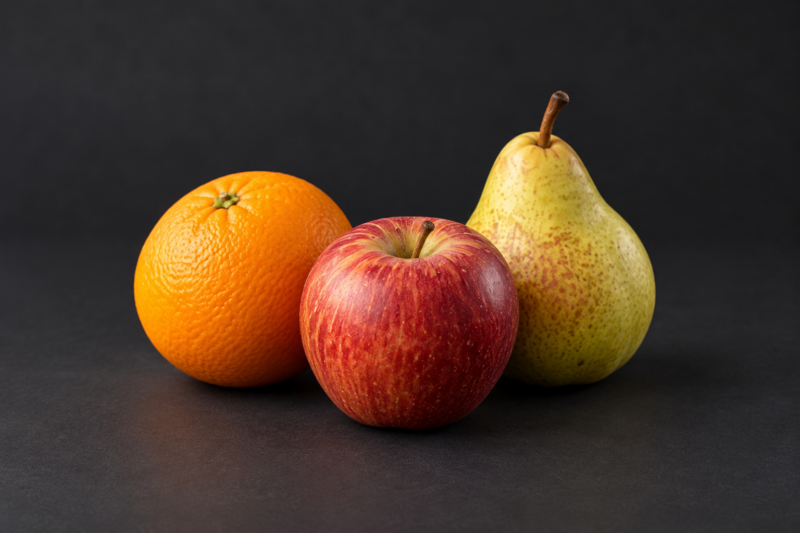 Une pomme, une orange et une poire sur fond sombre.
