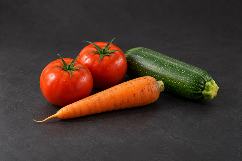 Deux tomates, une carotte et une courgette sur fond sombre.