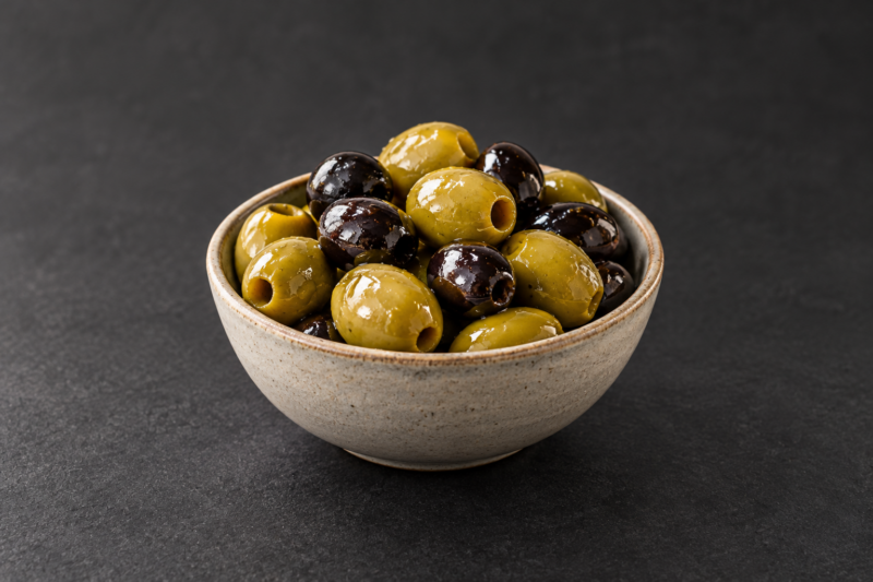 Un bol d’olives vertes et noires sur fond sombre.